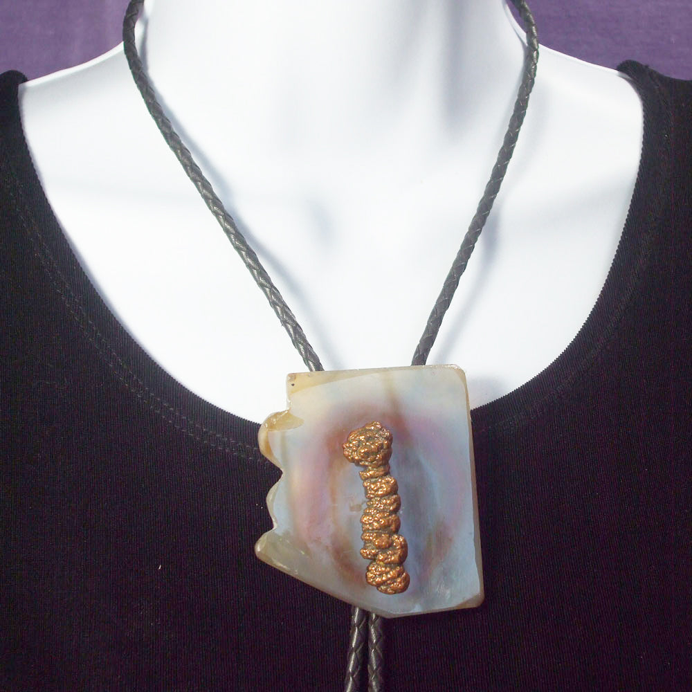 2 ½ inch by 2 ½ inch carved mineral shape of Arizona.  Jasper see thru with colored inclusion and a copper nodule attached to the top of Bolo Tie focal center.   Sterling Silver Bolo fastener and end cones.  