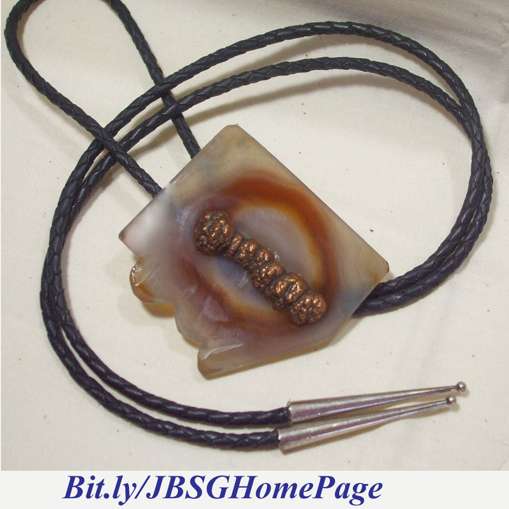 2 ½ inch by 2 ½ inch carved mineral shape of Arizona.  Jasper see thru with colored inclusion and a copper nodule attached to the top of Bolo Tie focal center.   Sterling Silver Bolo fastener and end cones.  