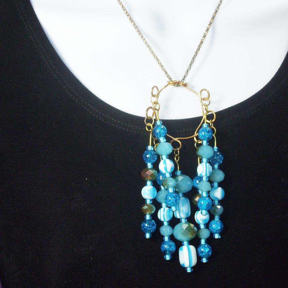 7 strands of various styles, cuts, shapes and textures of blue glass beads dangle on bronze wire from circular bronze wire design pendant.  Each strand giving a flash of color and blitz to this elegant necklace.